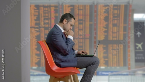 Foto Businessman sit on chair in airport and look busy at computer, timetable