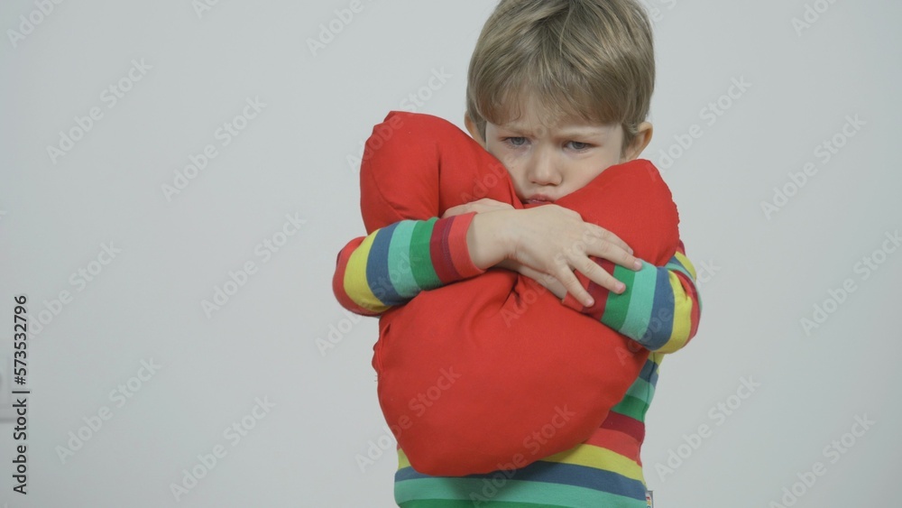 Cute boy hugging big red heart shaped pillow showing his love Cute boy hugging big red heart shaped pillow showing his love