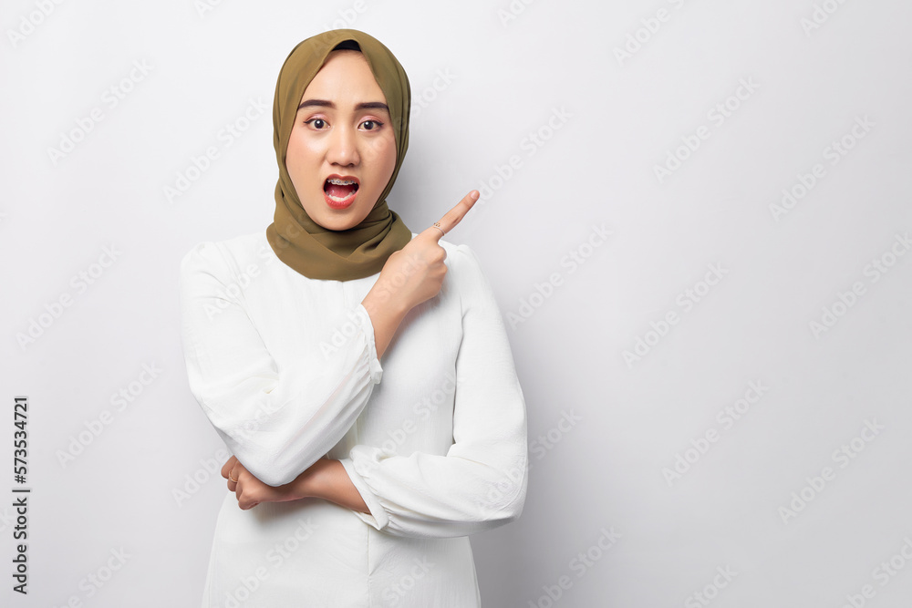 Beautiful shocked young Arabian Asian Muslim woman wearing hijab standing pointing finger at empty copy space isolated on white background. People religious lifestyle concept Beautiful shocked young Arabian Asian Muslim woman wearing hijab standing pointing finger at empty copy space isolated on white background. People religious lifestyle concept