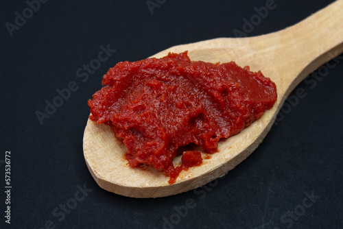 Wooden spoon with tomato paste on black background. Close up photo.