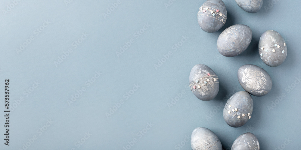 Festive Easter background. Gray-blue Easter eggs with stars on a blue table. Banner with a place for text. Top view. Festive Easter background. Gray-blue Easter eggs with stars on a blue table. Banner with a place for text. Top view.