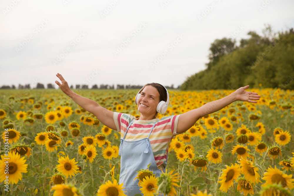 middle aged woman in headphones in a field with sunflowers at sunset. Audio healing. meditation. Amazing chill moment. banner Enjoying the little things. middle aged woman in headphones in a field with sunflowers at sunset. Audio healing. meditation. Amazing chill moment. banner Enjoying the little things.