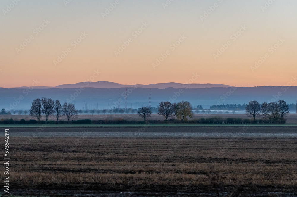 foggy sunrise over a field and mountains with leafy trees in a row in the Czech Republic