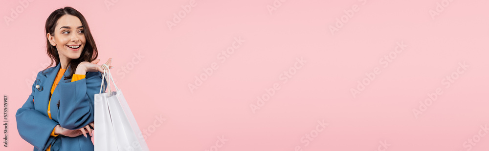 smiling young woman in blue blazer holding shopping bags isolated on pink, banner. smiling young woman in blue blazer holding shopping bags isolated on pink, banner.