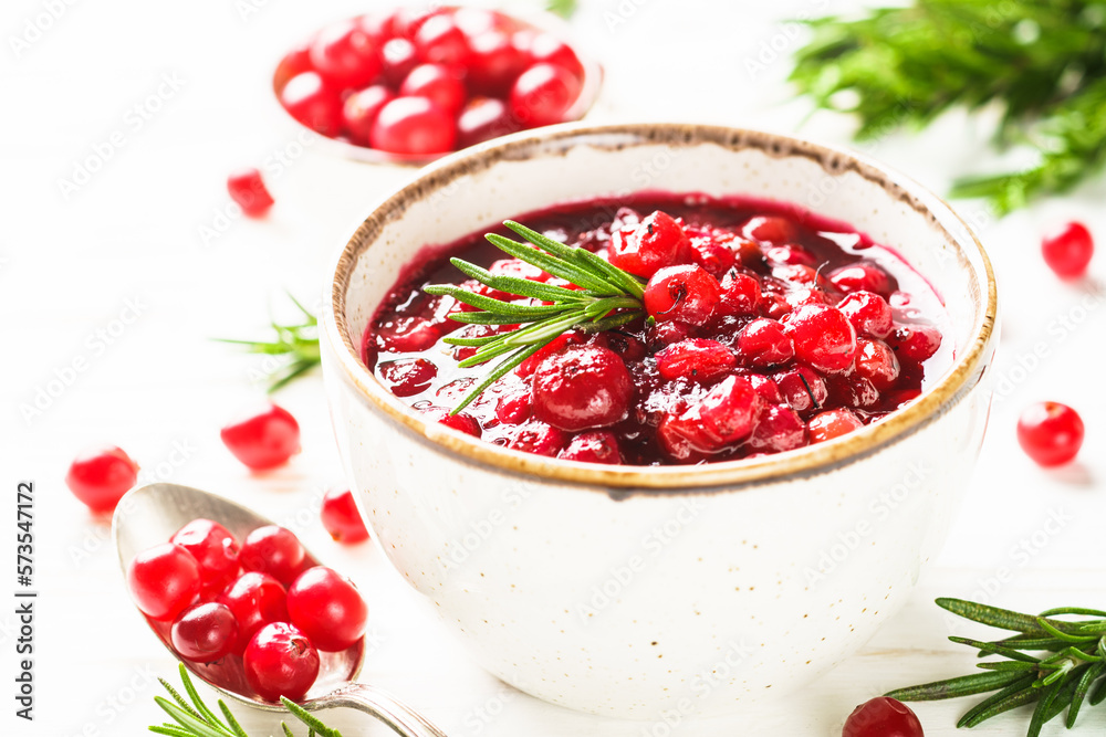 Cranberry sauce in craft bowl with rosemary at white table. Cranberry sauce in craft bowl with rosemary at white table.