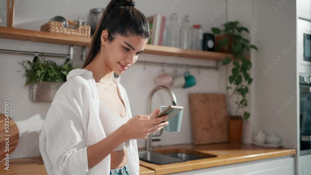 Video of beautiful woman taking selfies with her mobile phone while drinking a cup of coffee in the kitchen at home. Video of beautiful woman taking selfies with her mobile phone while drinking a cup of coffee in the kitchen at home.