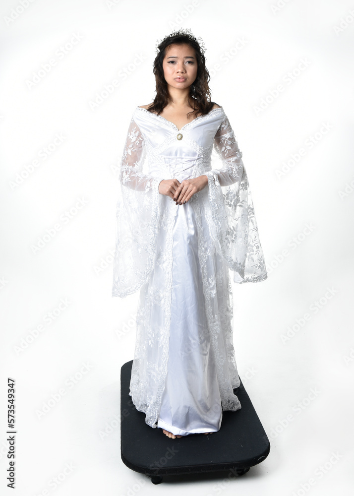 Full length portrait of beautiful woman wearing fantasy costume, white bridal gown. standing pose, gestural arm movements casting a spell. Isolated white studio background. Full length portrait of beautiful woman wearing fantasy costume, white bridal gown. standing pose, gestural arm movements casting a spell. Isolated white studio background.