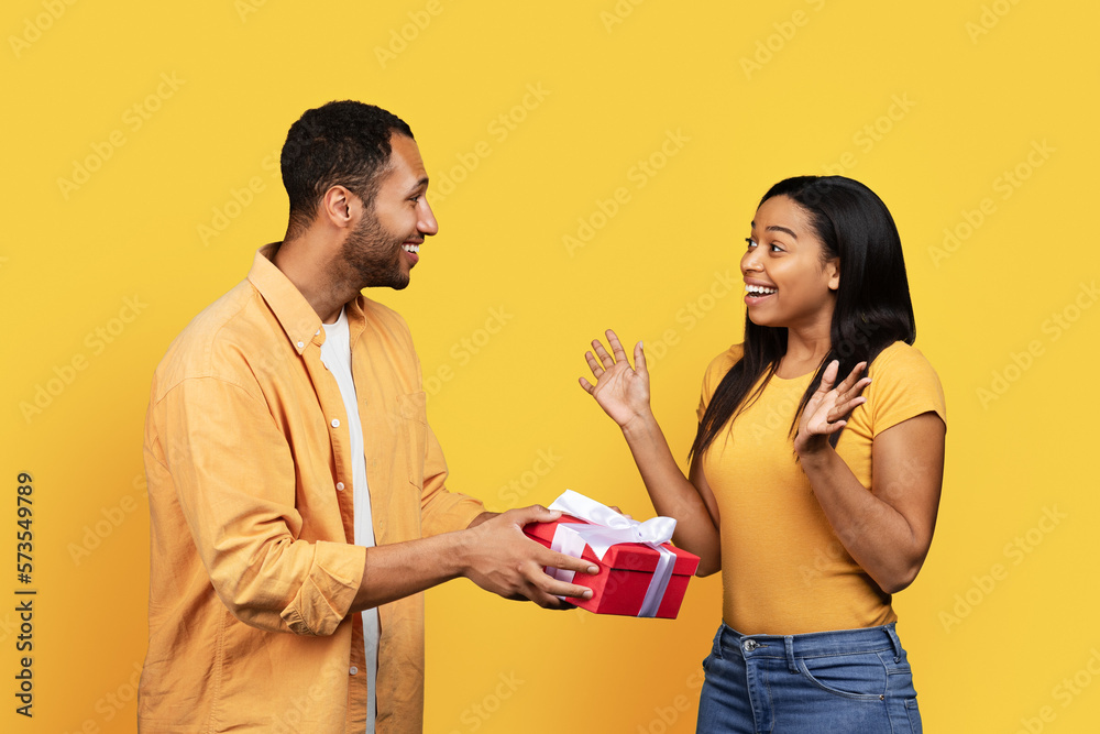 Smiling young african american guy give gift box to shocked woman, congratulate on holiday, anniversary Smiling young african american guy give gift box to shocked woman, congratulate on holiday, anniversary
