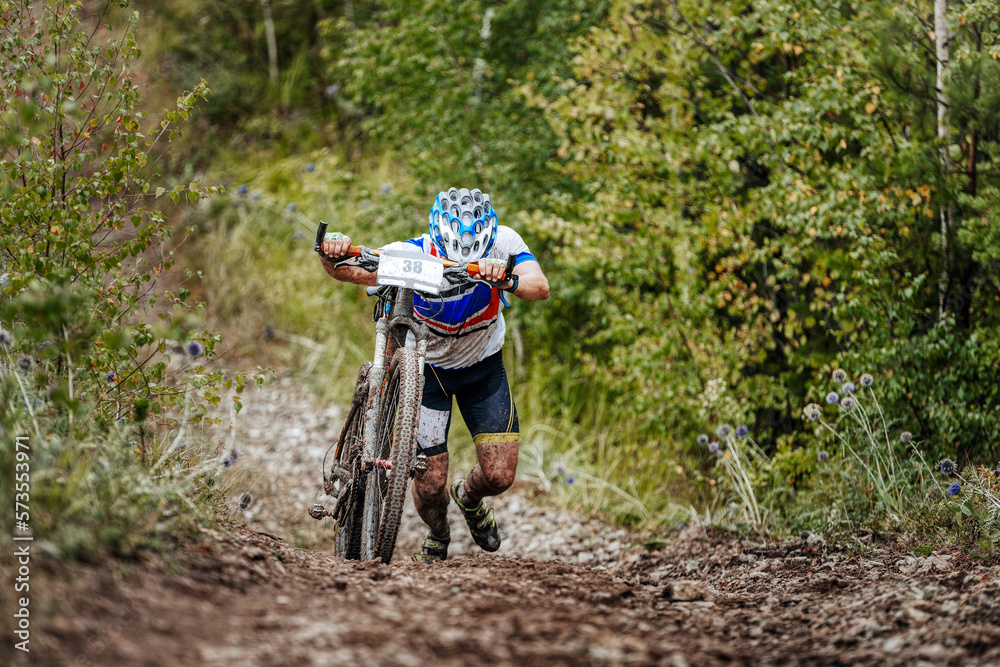 cyclist athlete with mountain bike walking uphill on forest trail cyclist athlete with mountain bike walking uphill on forest trail