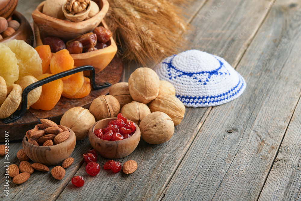 Fototapeta premium Tu Bishvat celebration concept. Mix of dry fruits and nuts almonds, hazelnuts, walnuts, apricots, prunes, cherries, raisins, dates, apples, figs over wooden table. Jewish holiday, new year of trees.