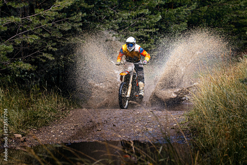 enduro racer riding on water with splashes motocross race in forest photo