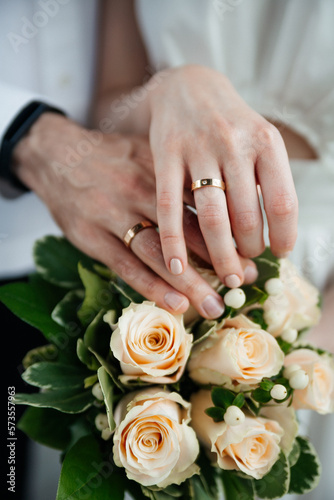 Hands of the bride and groom with rings after the wedding ceremony. Close up on the background of the bouquet