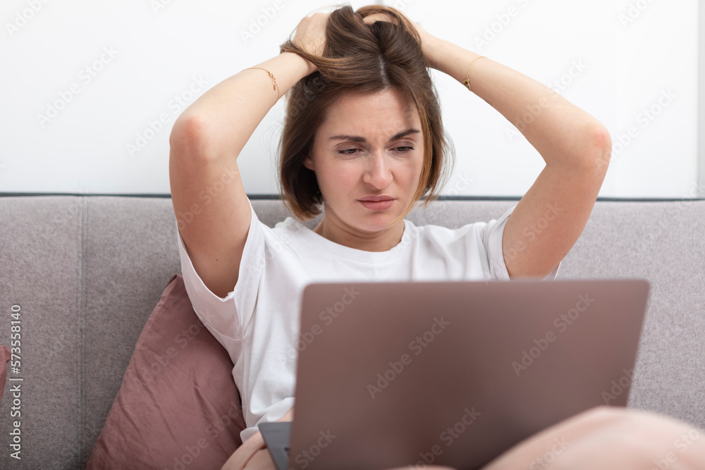 Shocked woman with hands on head working on laptop in the bed. Surprised and upset girl looking at her computer in the bedroom Shocked woman with hands on head working on laptop in the bed. Surprised and upset girl looking at her computer in the bedroom