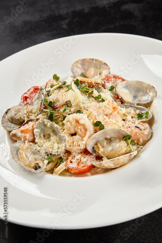 Seafood pasta with vongole, clams, salmon fish and prawns in white plate. Spaghetti marinara with seafood and cheese on dark background. Seafood menu -  pasta in mediterrian  style on black table.