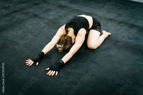 boxing woman wearing punching gloves bending body on ground. determined female athlete doing warm down or up. strong muscular gym trainer stretching bend body before exercise boxing sport training