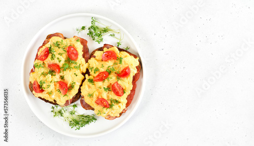 Scrambled eggs with microgreen, bacon and tomatoes on bread