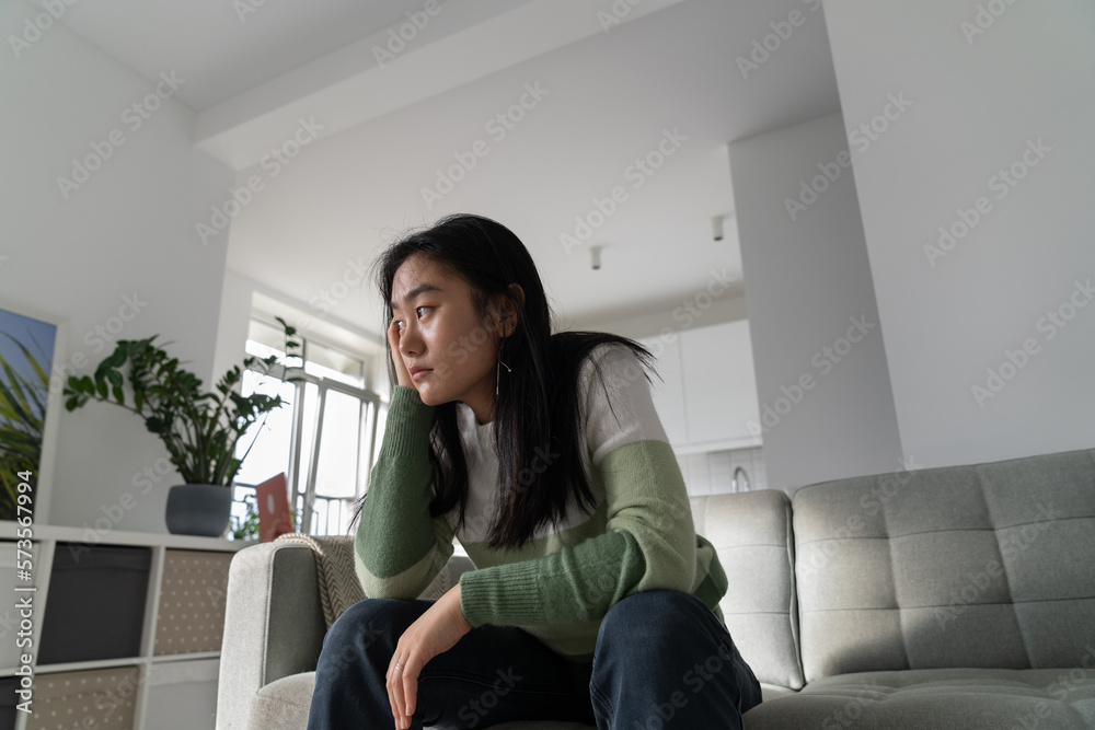 Unmotivated pensive Asian student girl sits on couch leaning head on hand. Procrastinating Chinese woman is stressed out because she doesnt want to start preparing for university entrance exams Unmotivated pensive Asian student girl sits on couch leaning head on hand. Procrastinating Chinese woman is stressed out because she doesnt want to start preparing for university entrance exams