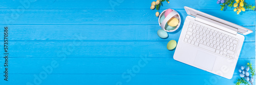 Easter office workplace, preparation for holiday, spring Easter sale, blogging. White laptop keyboard with easter eggs basket and flower branch decorations, on light blue wooden table top view 
