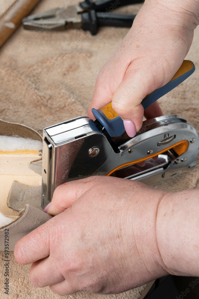 a woman works with a furniture stapler, a close-up view of her hand from above, upholstery of sofa parts, work in the workshop