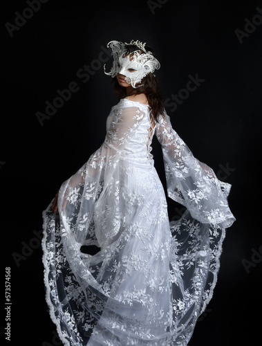  portrait of beautiful woman wearing white lace bridal fantasy gown with butterfly mask. isolated on black studio background.
