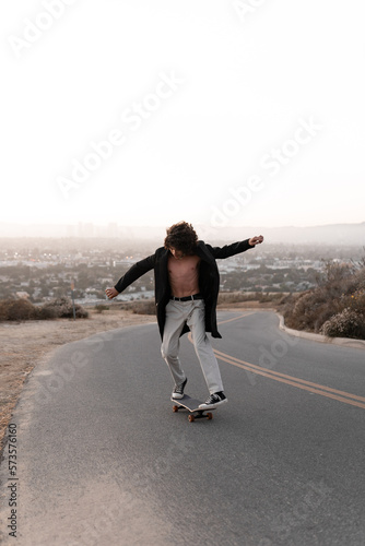 A shirtless young man wearing a gabardine is skating on a road in Baldwin Hills, Los Angeles