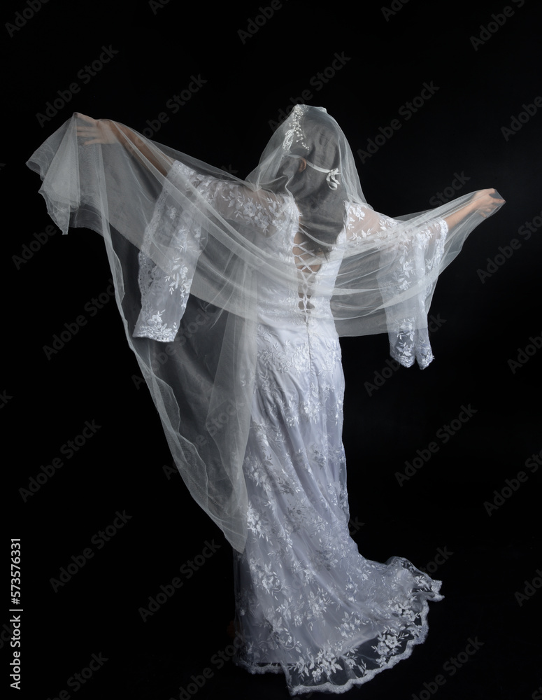 Full length portrait of beautiful woman wearing white bridal fantasy gown with butterfly mask and ethereal veil. Dancing with gestural arm poses, isolated on black studio background. Full length portrait of beautiful woman wearing white bridal fantasy gown with butterfly mask and ethereal veil. Dancing with gestural arm poses, isolated on black studio background.