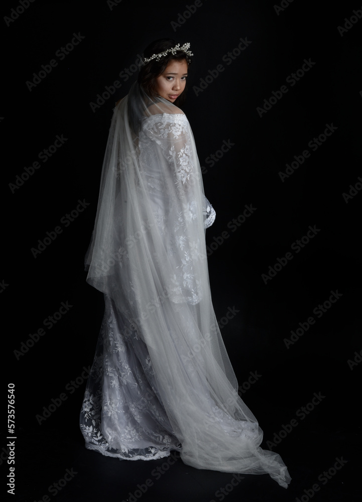 Full length portrait of beautiful woman wearing white bridal fantasy gown with butterfly mask and ethereal veil. Dancing with gestural arm poses, isolated on black studio background. Full length portrait of beautiful woman wearing white bridal fantasy gown with butterfly mask and ethereal veil. Dancing with gestural arm poses, isolated on black studio background.