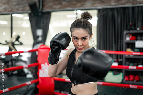 boxing confident woman punching wearing gloves. confident boxer coach training exercise to build muscle for body. determined tough female athlete trainer with gloves doing arms punching on gym ring