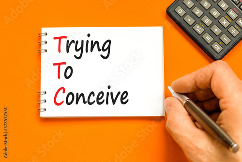 TTC trying to conceive symbol. Concept words TTC trying to conceive on white note on a beautiful orange background. Doctor hand. Medical and TTC trying to conceive concept. Copy space. photo