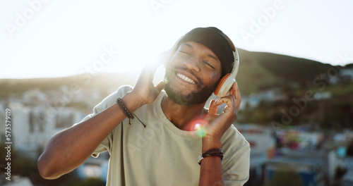 Man, music and dancing on rooftop with headphones in sunshine, city and summer with smile. Happy, black man and streaming to listen on internet, web or app to relax, dance and radio in Cape Town