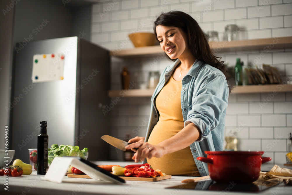 Young woman in kitchen. Beautiful pregnant woman making salad