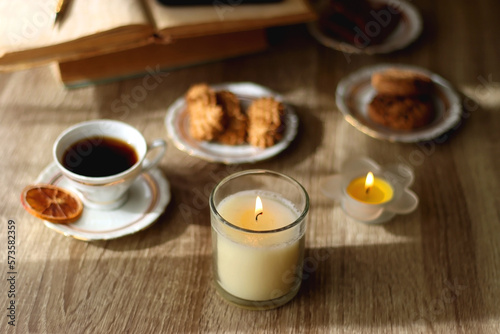 Scented candles, on the table. Selective focus.chocolate, cookies, cup of tea, books, e-reader, glasses and flowers on the table. Hygge at home. Selective focus.