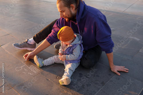 Dad and child draw with chalk on the pavement.