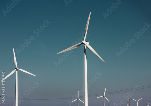 Windmills against a dramatic blue sky. Renewable energy production, ecology, alternative electricity concept. Green technology. Windfarm with white propellers. Wind mills industry. Power and energy. © vita