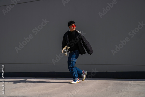 young asian man with cool red glasses running with skateboard in hand smiling urban lifestyle