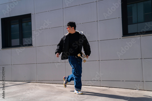 young asian man with cool red glasses running with skateboard in hand smiling urban lifestyle