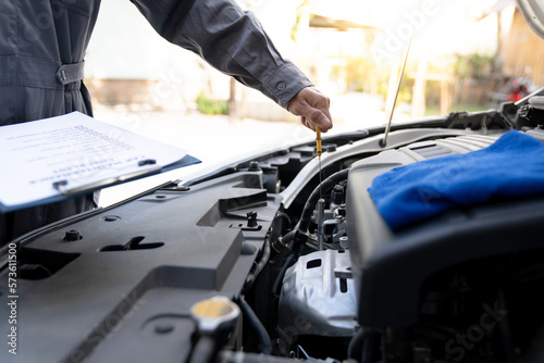 Maintenance engineer or auto mechanic pulls engine oil dipstick to inspect and check mileage of car, oil change ready to check information Enter record details in the car maintenance service file. © crizzystudio