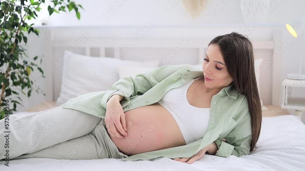 A pregnant woman with a large open belly strokes her stomach and dreams of having a baby. The expectant mother is waiting and preparing for the birth of a child at home in a bright children's bedroom. A pregnant woman with a large open belly strokes her stomach and dreams of having a baby. The expectant mother is waiting and preparing for the birth of a child at home in a bright children's bedroom.