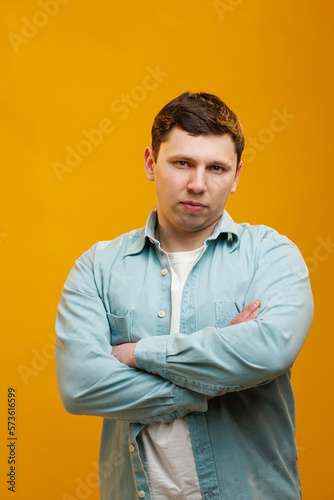 Portrait of handsome european man in shirt looking at camera standing on yellow studio background