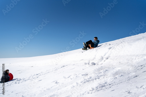 Cute young boy sprayed with snow as he is sledging down a hill