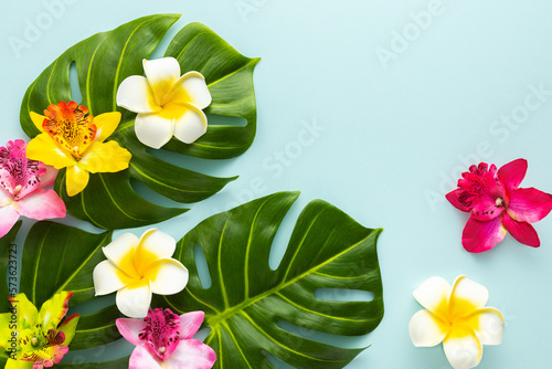 Summer background with tropical orchid flowers and green tropical palm leaves on light background. Flat lay, top view. Summer party backdrop