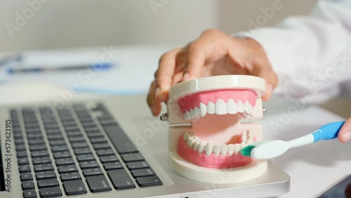 Dentist teaching explaining how to brush teeth correctly to patient after treatments on doctor desk with laptop computer, tutorial showing instructional brushing movements teeth clean dental hygiene