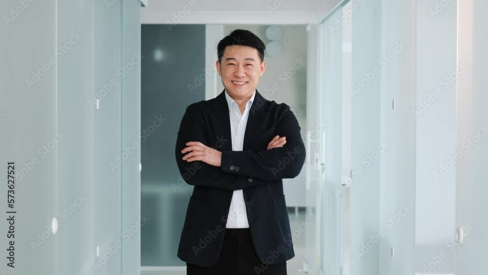 Smiling confident young professional asian business man turning head looking at camera crossing hands in office hallway. Portrait of positive male korean person dressed in stylish formal clothes. Smiling confident young professional asian business man turning head looking at camera crossing hands in office hallway. Portrait of positive male korean person dressed in stylish formal clothes.