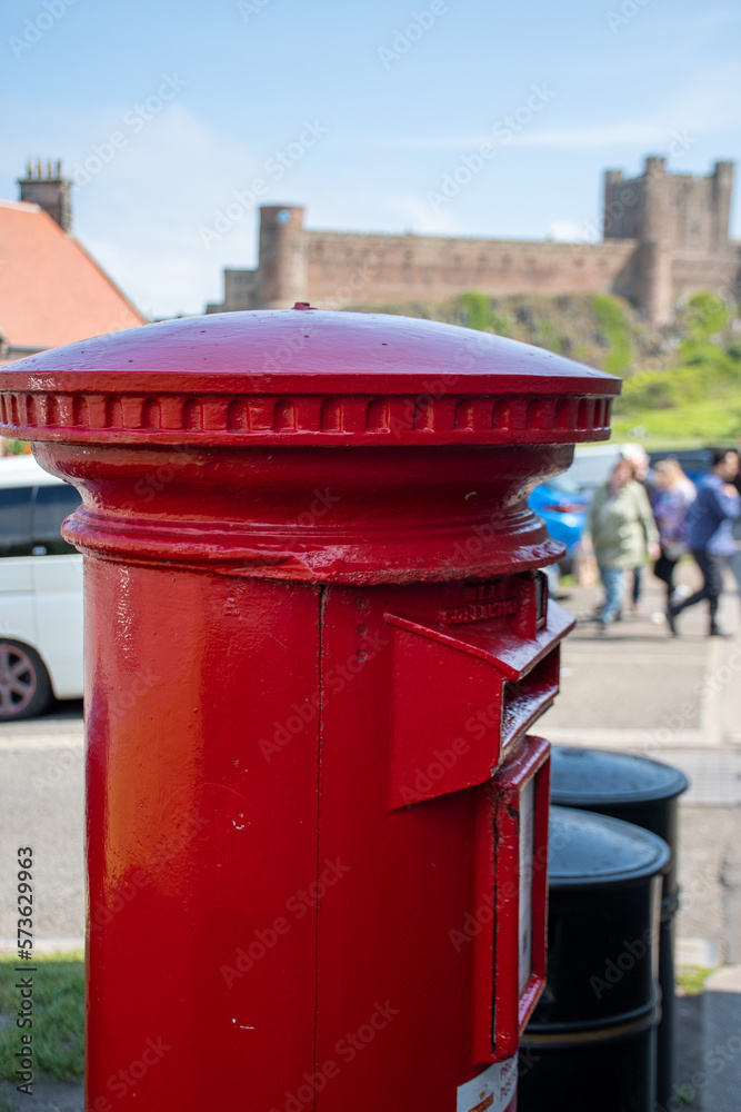 Traditional red post box in Bamburgh village, Northumberland. With out of focus castle in background Traditional red post box in Bamburgh village, Northumberland. With out of focus castle in background