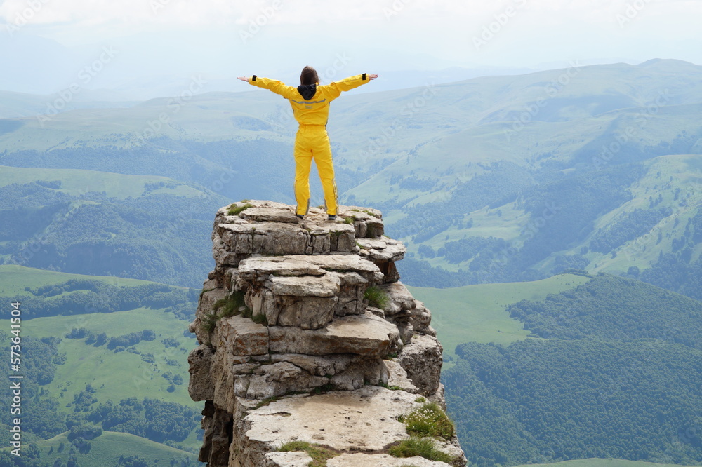 Obraz premium Tourist girl near Elbrus at Bermamyt plateau, Karachay Cherkessia. Happy hiker standing on a rock with her arms outstretched, freedom and happiness, achievement in mountains