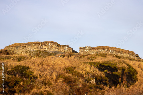 Ruins of ancient fortress on a hill in sunlight with yellow dry grass. photo