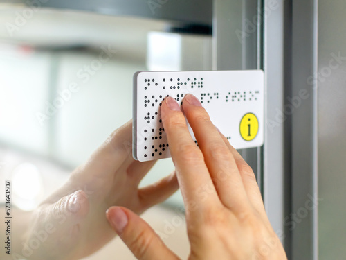 Person with blindness touches and reads with his hands the Braille text plate on the door of a train or bus. Close-up of fingers touching the relief of points in transport. Sightless, low vision.