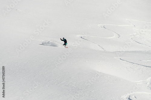 awesome beautiful view of a snow-covered mountain slope and a man on a snowboard speedly slides down. Freeride concept
