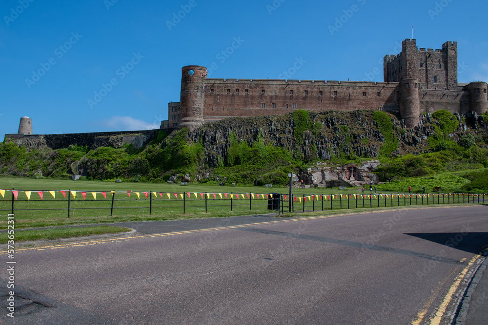 View of Bamburgh Castle from the road, against a bright blue summer sky. Northumberland, UK. Platinum Jubilee bunting on nearby fence. Summer 2022