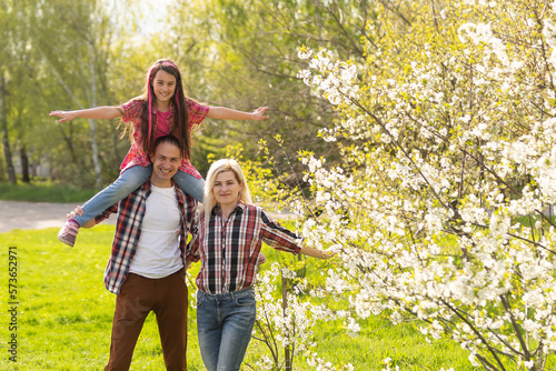Happy parents mom and dad, daughter, young family outdoors in spring against the background of blooming apple and cherry trees